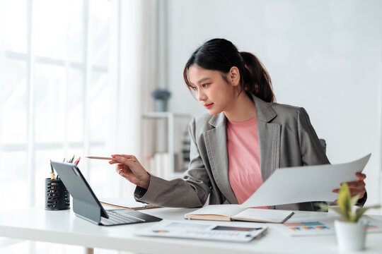 Young professional woman pointing at tablet screen and reviewing paperwork, focused on financial analysis and business strategy