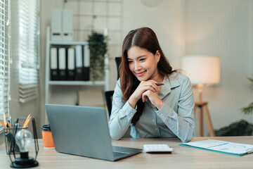 Obraz premium Young happy Asian businesswoman working from home office using laptop computer and smiling, startup, small business owner, e commerce, online business
