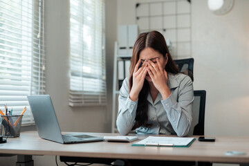 Businesswoman suffering from headache and eye strain after working on laptop for a long time in office
