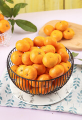 Fresh Small Satsuma Tangerines in Wire Basket on Marble Plate with Green Leaves