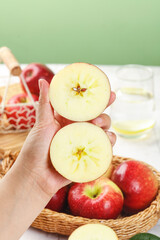Fresh Red Apple Halves Showing Star Core Pattern in Hand with Basket of Apples on Kitchen Table