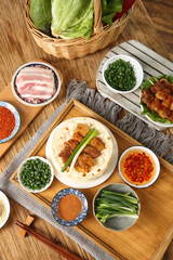 Asian BBQ feast with grilled meat wraps vegetables and traditional condiments on wooden table