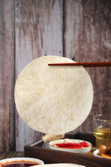 Wheat flour tortilla with chopsticks and Asian condiments on rustic wooden background