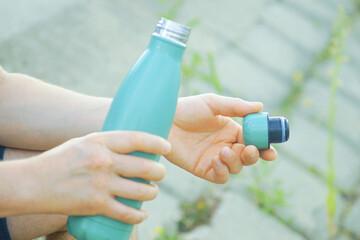 Individual about to hydrate with reusable metal thermo bottle in outdoor setting. Drinking preparation and hydration moment capture. Symbolizes ready for consumption, refreshment access, thirst relief