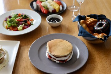 Breakfast spread on a restaurant or cafe table including pancake, salad, fruits etc