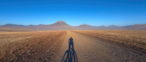 Cyclist shadow long dusty path desert sunrise landscape mountain silhouette, calm mood and wide horizon view