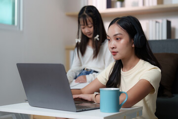 Focused Learning. Young woman working on a laptop while her sister observes.