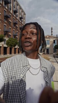 Vertical POV shot of male African American zoomer in streetwear drinking cocktail and talking on camera on city street