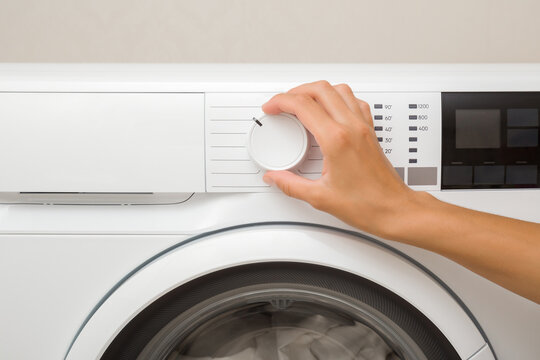 Young adult woman hand finger turning button on white washing machine. Setting temperature or functions for clothes washing. Choosing program for water or energy saving. Closeup. Front view.