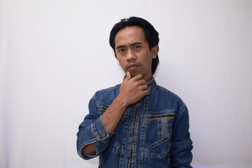 a blurry photo of a Southeast Asian man in Levis jacket, holding his beard with thoughtful and analyzing expression