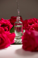 A dropper releases a few drops of oil into a small glass bottle surrounded by vibrant pink roses....