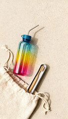 Eco-Friendly Essentials: A colorful water bottle with reusable metal straw, sustainable wooden toothbrush, and a linen pouch on a sandy surface.