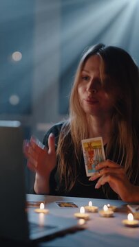 Young woman holding tarot card during fortune telling ritual with candles
