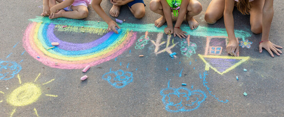 Children draw a picture with chalk on the asphalt. A rainbow, a house are drawn on the asphalt.