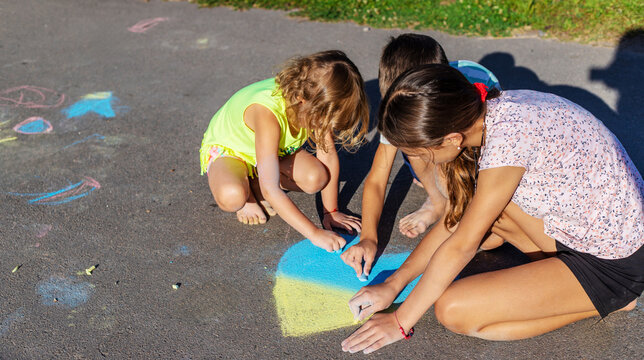 Children draw a heart with chalk and color it in blue and yellow.