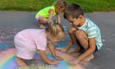 Children draw with chalk on the asphalt.A rainbow, a house, the sun, clouds are drawn on the asphalt
