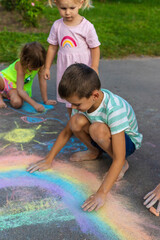 Children draw with chalk on the asphalt.A rainbow, a house, the sun, clouds are drawn on the asphalt