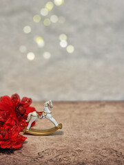 Vintage Christmas background with small white ceramic rocking horse and red flowers, soft bokeh lights and space for text.