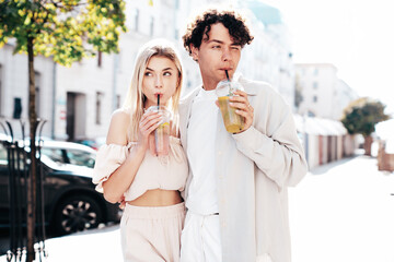 Young smiling beautiful woman and her handsome boyfriend in casual summer clothes. Happy cheerful family. Female having fun. Couple posing in street. Holding and drinking cocktail drink in plastic cup