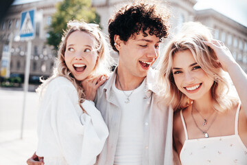 Young three stylish friends posing in the street. Fashion man and two cute female dressed in casual summer clothes. Smiling models having fun. Cheerful women and guy outdoors, in sunny day