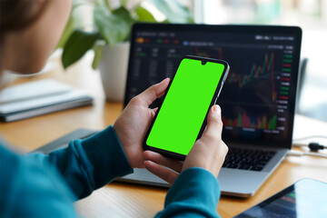 Person Using Green Screen Smartphone with Stock Market Charts on Laptop – Financial Technology Concept