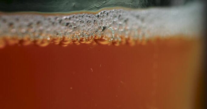 Close-up of Kombucha fermentation bubbling in a glass container. See the fizzy bubbles and natural process of making this trendy, healthy, and delicious fermented tea drink at home.
