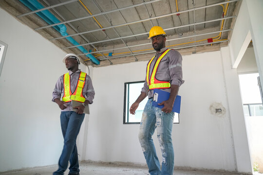 Two construction workers inspecting a site in a new building under construction in bright sunlight - Powered by Adobe