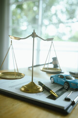 A symbolic scene featuring the scales of justice, a car, a hammer and contract documents representing law, insurance, judgment and legal liability in the event of an accident.