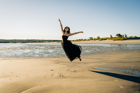 Ballerina jumping on the beach at sunset wearing flowing black dress