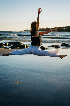 Young ballerina performing splits jump on the beach at sunset