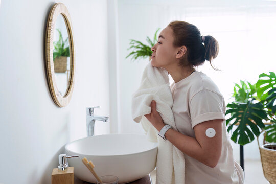 Woman with diabetes cleaning face with towel in bathroom at home