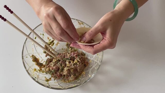 Hands making steamed buns with fresh meat and vegetable filling. Traditional homemade cooking scene showing dough wrappers, savory stuffing, and step-by-step preparation.