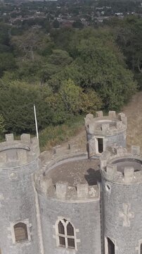Vertical aerial drone footage at Blaise Castle, Henbury, Bristol. It begins close above the three turrets, reversing and rising to show the castle grounds, surrounding woodland, and urban landscape.