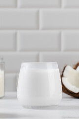 Fresh coconut milk in glass with sliced coconut and white tile background. Alternative milk