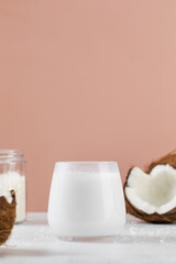 Fresh coconut milk in glass with sliced coconut on pink background. Alternative milk