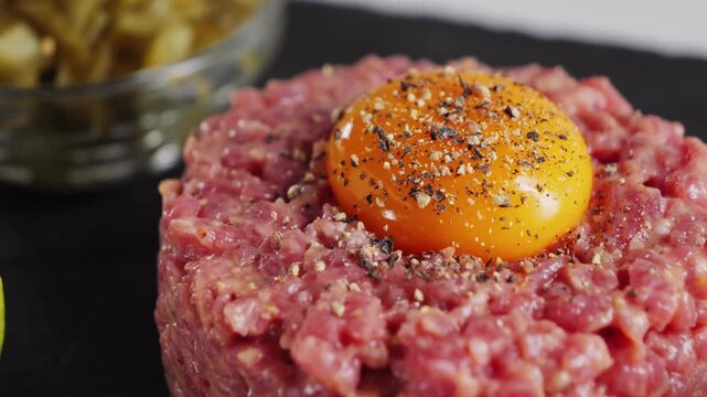 Raw beef tartare with sauce on a black stone tray. Homemade tartare with onion, capers, and egg yolk. High-quality 4K video. High quality 4k footage