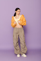 Fototapeta premium A beautiful young woman showcases her fashion sense with a bright orange jacket and relaxed pants.