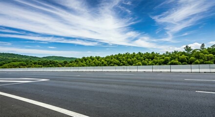 Naklejka premium Empty highway stretches into a lush green hillside under a vibrant blue sky