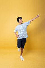 Enthusiastic young person with headphones pointing upwards against yellow background Energy in youth