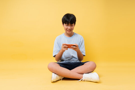 Young person is absorbed in a cell phone game seated against vibrant yellow background