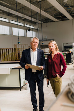 Businessman by businesswoman standing with hand in pocket at factory
