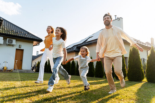 Happy family running in the garden of their house with solar panels
