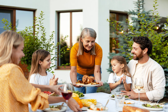 Beautiful grandmother serving roasted chicken to family at garden, festive dinner