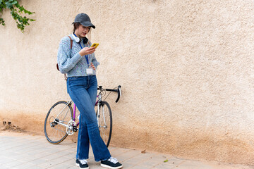 Young woman using smartphone next to her bicycle leaning against a wall