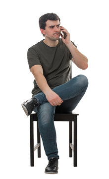 Dissatisfied young man sitting on chair talking on phone. Thoughtful male seated full length portrait isolated on transparent background