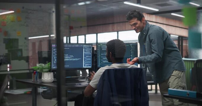 Two Professional IT Programers Discussing Blockchain Data Network Architecture Design and Development Shown on Desktop Computer Display. Caucasian and a Black Man Working in a Technical Department