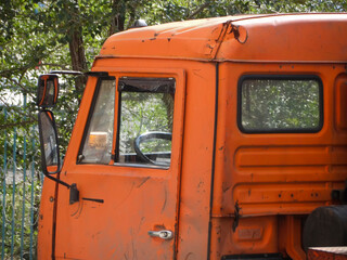 Close-up of rusty and dented orange KAMAZ 6520 truck cabin. Old worn industrial vehicle with damaged bodywork, visible scratches and corrosion, showing signs of long service and heavy use.