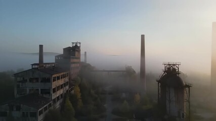 Drone footage capturing an aerial view of an abandoned industrial factory shrouded in morning mist at dawn, urban decay concept. - Powered by Adobe
