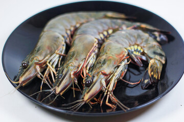 3 Black Tiger Prawns on a Black Plate, on a White Background
