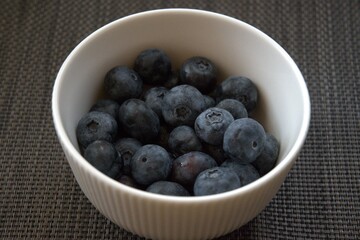 Fresh ripe blueberries in a white ceramic bowl with gray background, close-up shot with copy space for text.